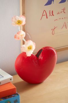 a red heart shaped vase sitting on top of a table next to books and a laptop