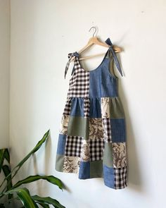 a patchwork dress hanging on a wall next to a potted plant