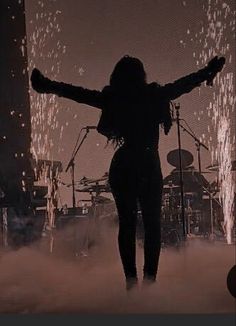 a woman standing on top of a stage with her arms outstretched in front of fireworks