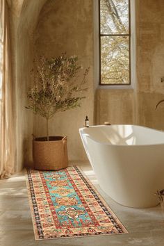 a bath tub sitting next to a white sink under a window in a bathroom with a rug on the floor