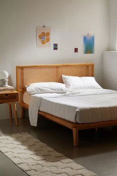 a bed with white sheets and pillows in a room next to a table, lamp and window