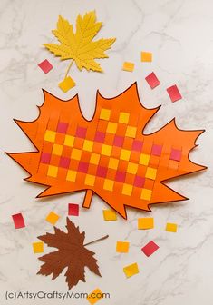 an orange and yellow leaf cut out on a marble surface with fall leaves scattered around it