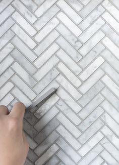 someone is cutting through the white marble herringbone pattern with a scissor knife