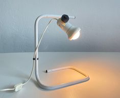 a white desk lamp sitting on top of a table next to a light plugged in