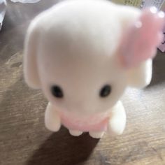 a small white stuffed animal with a pink bow on it's head sitting on a table