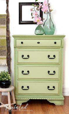 a green dresser with pink flowers on top and a black framed picture above it, against a white wall