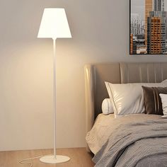 a white floor lamp sitting on top of a bed next to a night stand and pillows