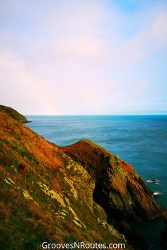 an ocean cliff with grass and rocks on the side, under a blue sky that has clouds in it