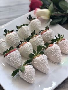 strawberries are arranged on a white platter with flowers in the backgroud