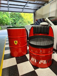 two red barrels sitting on top of a checkered floor next to a white car