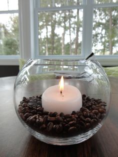 a lit candle in a glass bowl filled with coffee beans on a table next to a window