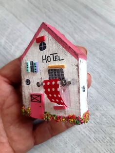 a hand holding a small wooden house with the word hotel painted on it's side