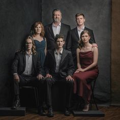 a group of people sitting next to each other in front of a black background with one woman wearing a red dress