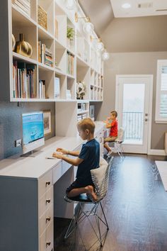 two young boys sitting at a desk in front of a computer monitor and bookshelf