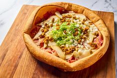 a wooden cutting board topped with a pizza covered in toppings and meat on top of it