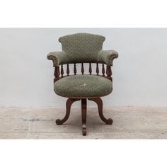 an old chair with a green upholstered back and arm rests against a white wall