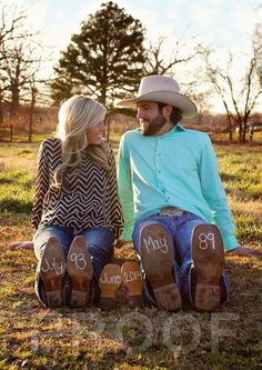 a man and woman sitting on the ground with their feet up to each other, wearing cowboy hats