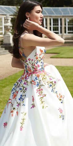 a woman in a white dress standing on grass with her hands behind her head and looking off to the side