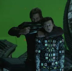 two men standing next to each other in front of a green screen with lights on