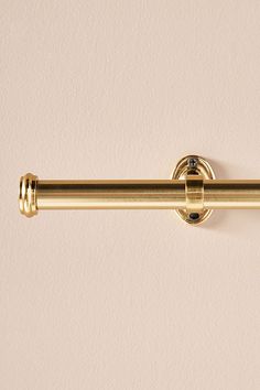 a close up of a metal curtain rod on a wall with a light pink background