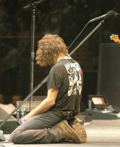 a man sitting on the ground with his guitar in front of him and microphone behind him