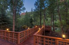 a wooden bridge surrounded by trees with lights on it's sides and some rocks in the background