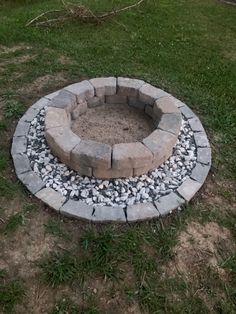 a stone fire pit in the middle of some grass