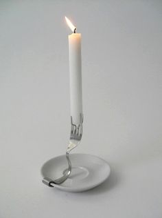 a single white candle on a plate with a fork sticking out of the center,