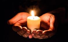 two hands holding a lit candle in the dark