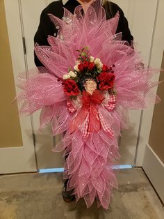 a woman standing in front of a door holding a pink wreath with flowers on it