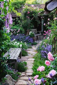 a garden with pink and purple flowers, benches and stone path leading up to the house