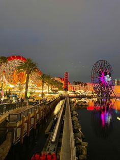 an amusement park at night with ferris wheel and lights on the water's edge