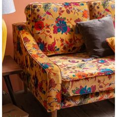 a yellow floral couch with two pillows on top of it and a lamp next to it