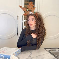 a woman with long curly hair sitting at a counter wearing reindeer antlers on her head