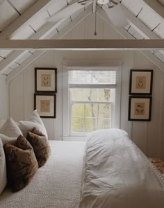 a white bed sitting under a window in a bedroom next to a wooden floor and ceiling