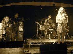 three people on stage playing instruments and singing with one woman standing in front of them