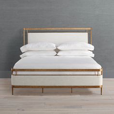 a bed with white linens and gold frame against a gray wall in a bedroom