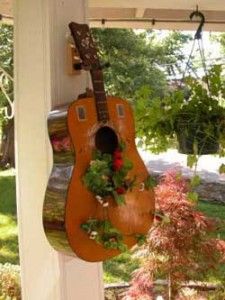 a guitar hanging from the side of a house with flowers in it's mouth