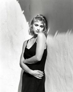 a black and white photo of a woman leaning against a wall with her arms crossed