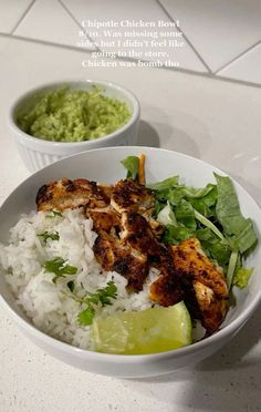 two white bowls filled with rice and chicken next to a lime wedge on the side