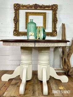 a white table with two vases on it and a gold framed mirror behind it