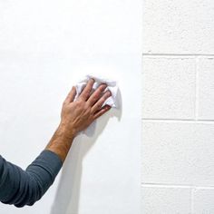 a person wiping up a white wall with a cloth on the edge and a hand holding a rag over it