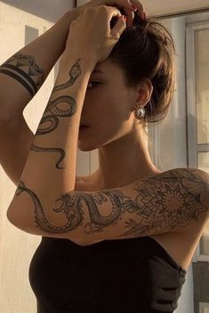 a woman with tattoos on her arms and arm is looking at the camera while standing in front of a window