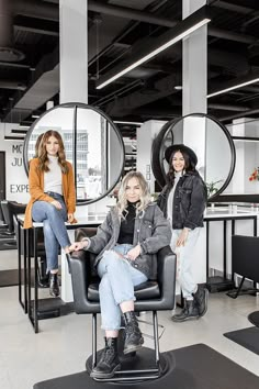 three women sitting on chairs in an office with round mirrors behind them and one woman standing next to the chair