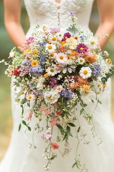 a bride holding a bouquet of wildflowers and daisies in her hands,