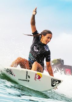 a woman riding a surfboard on top of a wave in the ocean with her arms up