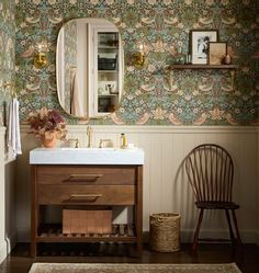 a bathroom with a sink, mirror and wooden chair in front of the wallpaper