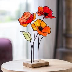 three red and yellow flowers sitting on top of a wooden table next to a window