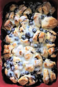 blueberry bread pudding in a red casserole dish with white icing on top