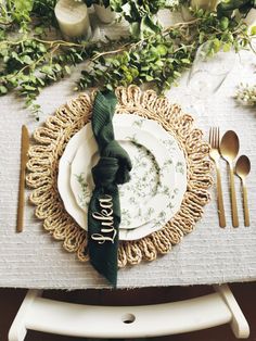 a place setting with plates, silverware and greenery